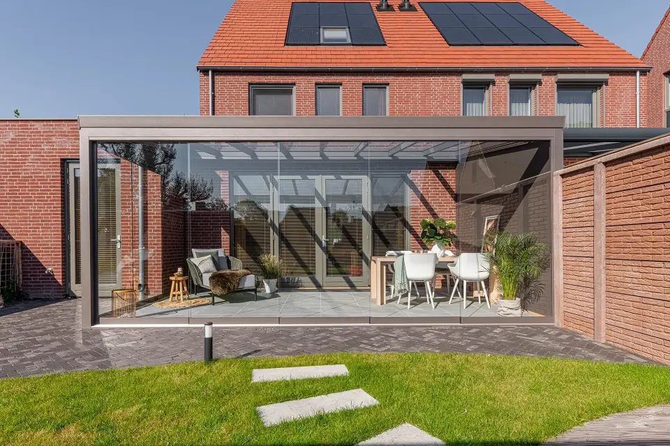 Moderne tuinkamer met glazen schuifwanden en aluminium constructie, aangebouwd aan een woning, ingericht met een zit- en eethoek.