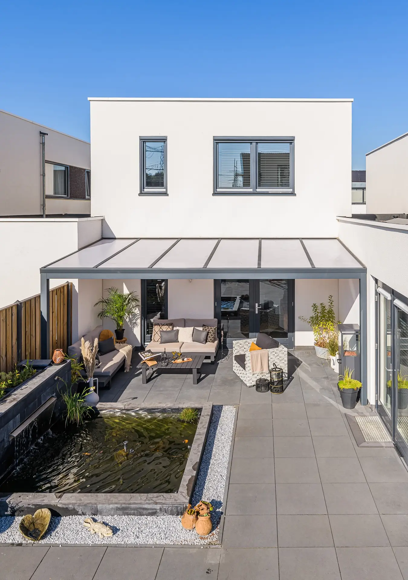 Verasol overkapping met polycarbonaat dak en moderne loungeset aan vijver.